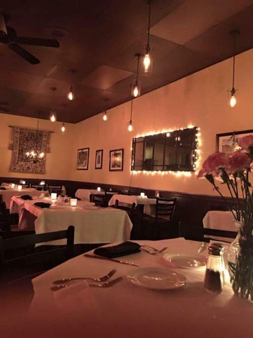 Cozy restaurant interior with dim lighting, white tablecloths, and floral centerpieces, creating an inviting atmosphere.