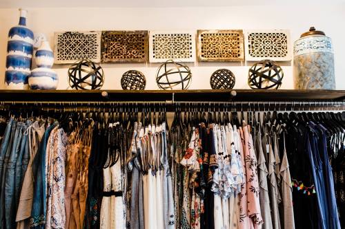 A clothing rack filled with various dresses and tops, decorated with artistic objects on a shelf above.