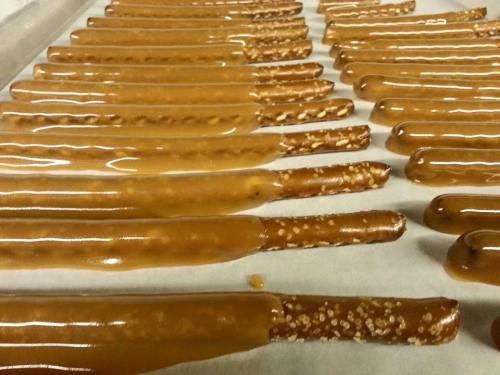 Rows of pretzel sticks coated in a shiny layer of caramel on a baking sheet.
