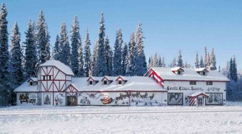 A snowy landscape featuring a festive building decorated with holiday murals, surrounded by tall evergreen trees.