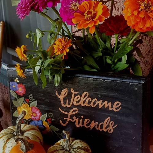 A decorative sign reading "Welcome Friends" surrounded by colorful flowers and pumpkins.