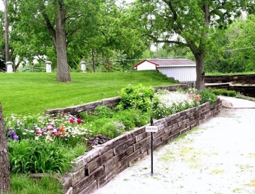 A lush garden with colorful flowers and a grassy area, bordered by wooden retaining walls and trees in the background.