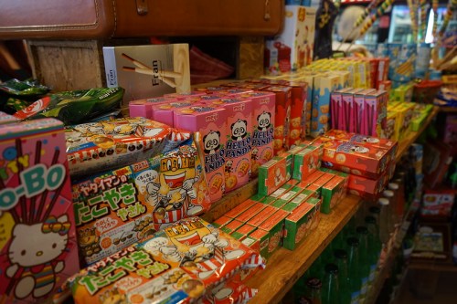 Colorful assortment of candy boxes and snacks displayed on wooden shelves in a shop.