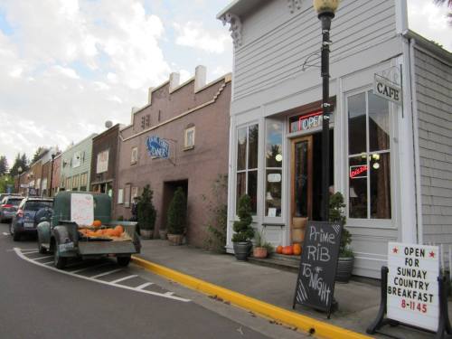 A quaint street scene featuring a diner, cafe, and shops, with pumpkins for sale outside and a vintage truck parked nearby.