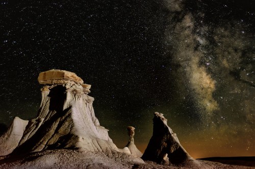 A starry night sky over unique rock formations, with the Milky Way visible in the background.