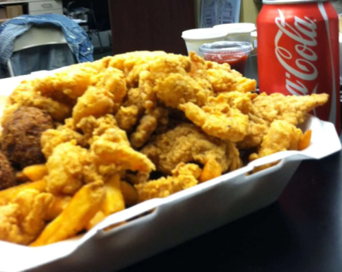 A large serving of fried chicken and fries in a takeout container, with a can of Coca-Cola nearby.