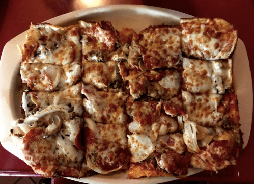 A rectangular platter of sliced pizza topped with cheese, pepperoni, mushrooms, and various other toppings.