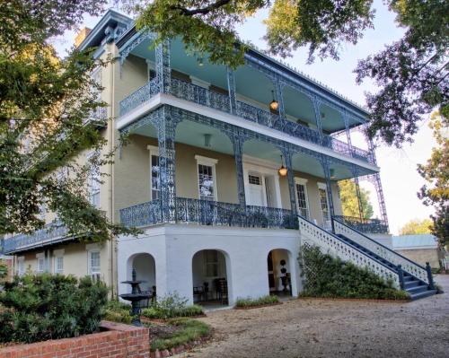 Historic three-story house with blue balconies, white columns, and a gravel pathway surrounded by greenery.
