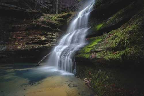 A serene waterfall cascades over moss-covered rocks into a tranquil pool, surrounded by lush greenery.