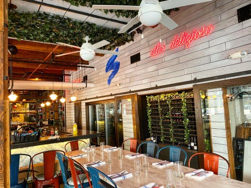 A modern restaurant interior with a long table, colorful chairs, and a neon sign reading "cibo delizioso."