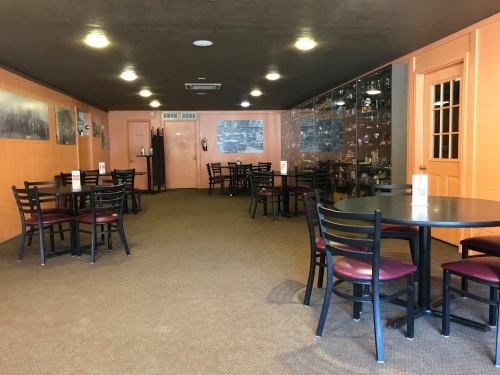 Interior of a restaurant with empty tables and chairs, orange walls, and a display case in the background.