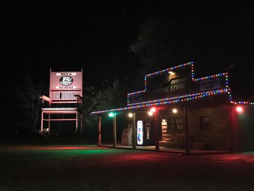 A brightly lit general store at night, adorned with colorful lights, next to a large sign for "Rodeo 66."