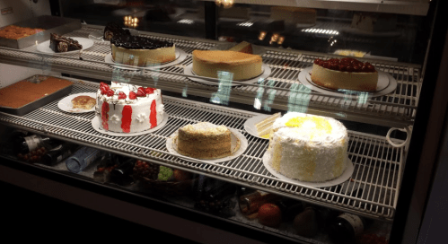 A display case filled with various cakes, including fruit-topped, chocolate, and cream cakes.