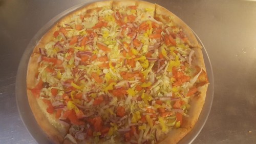 A freshly baked pizza topped with lettuce, tomatoes, onions, and yellow peppers on a golden crust.