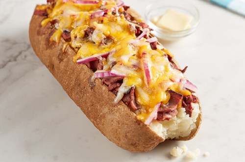 A loaded baked potato topped with melted cheese, chopped onions, and served with a side of butter.