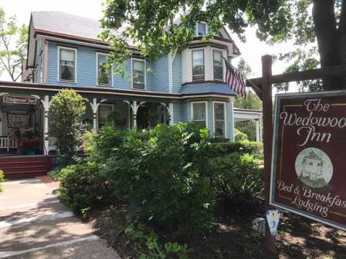 A charming blue Victorian house with a sign for "The Wedgwood Inn" and lush greenery in the foreground.