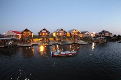 A serene waterfront scene featuring stilted houses and a small boat on calm water at dusk.