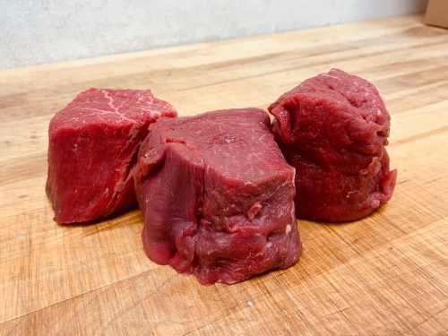 Three pieces of raw red meat on a wooden cutting board.