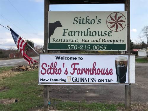 Sign for Sitko's Farmhouse restaurant, bar, and banquets, featuring Guinness on tap, with an American flag nearby.