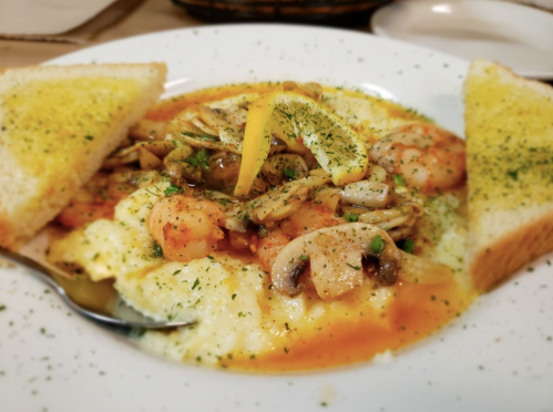 A plate of shrimp and grits topped with herbs, served with two slices of buttered toast and a lemon wedge.