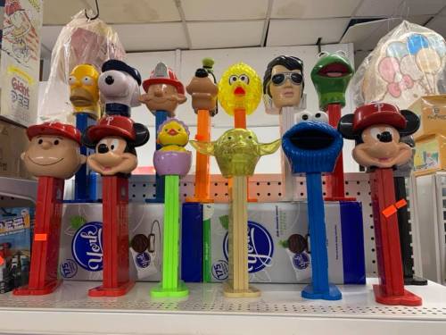 A colorful display of various character-themed PEZ dispensers on a shelf, featuring iconic cartoon and movie figures.