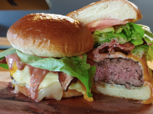 A close-up of a juicy burger with lettuce, tomato, cheese, and bacon, served on a toasted bun.