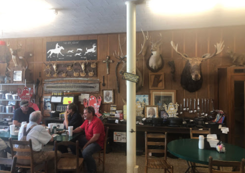 A rustic diner with wooden walls, mounted animal heads, and patrons sitting at tables enjoying their meals.