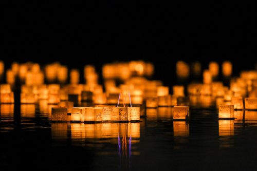 Floating lanterns illuminate a dark water surface, creating a serene and magical atmosphere.