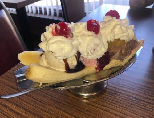A banana split topped with whipped cream and cherries, served in a silver dish on a wooden table.
