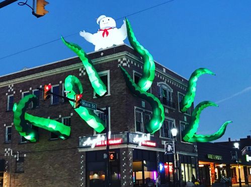 A building at dusk features a giant Stay Puft Marshmallow Man and green tentacles emerging from the roof.