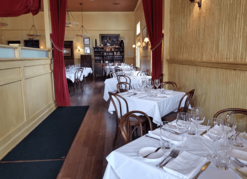 Elegant restaurant interior with white tablecloths, wooden chairs, and red curtains, creating a warm, inviting atmosphere.