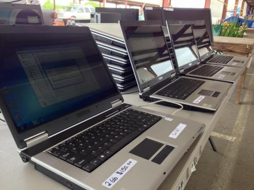 A row of laptops on a table, each with a price tag, in a market setting.