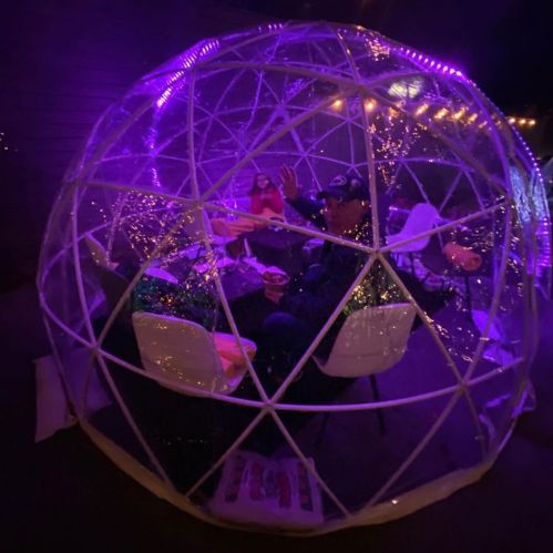 A cozy, illuminated dome with people sitting inside, surrounded by twinkling lights and festive decor.