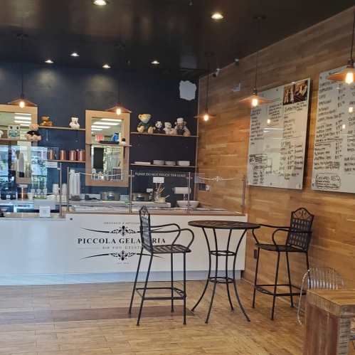 Interior of Piccola Gelateria featuring a counter, menu board, and seating area with wooden accents and warm lighting.