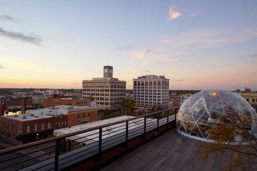 A city skyline at sunset, featuring buildings and a transparent dome structure on a rooftop.
