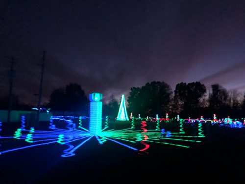 A colorful display of holiday lights in various shapes, set against a darkening sky.
