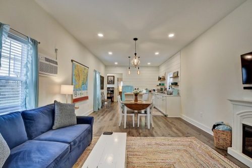 Cozy living space featuring a blue sofa, dining area, and modern kitchen with light wood flooring and bright decor.