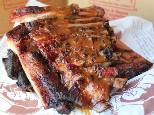 A close-up of succulent, glazed barbecue ribs stacked on parchment paper, showcasing a rich, smoky sauce.