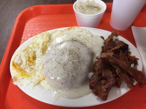 A plate of eggs topped with gravy, crispy bacon, and a cup of white beverage on a red tray.