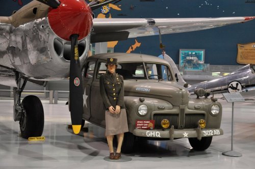 A vintage military truck and a life-sized soldier statue in front of a WWII aircraft in a museum setting.