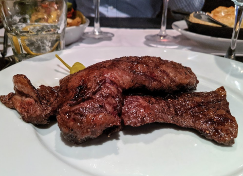 A close-up of two pieces of grilled meat on a white plate, garnished with a green olive.