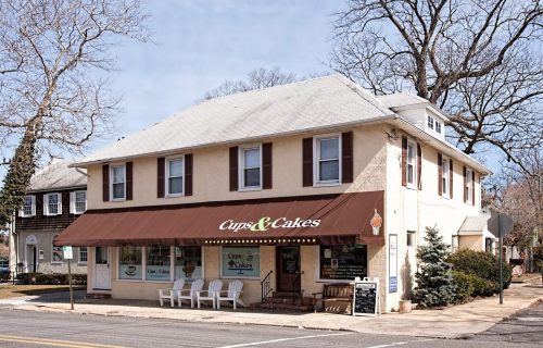 A quaint bakery named "Cups & Cakes" with a brown awning, located in a two-story building on a quiet street.