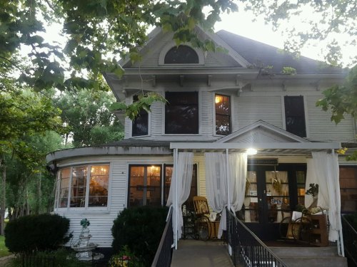 A charming two-story house with large windows, a porch, and greenery, illuminated in the evening light.