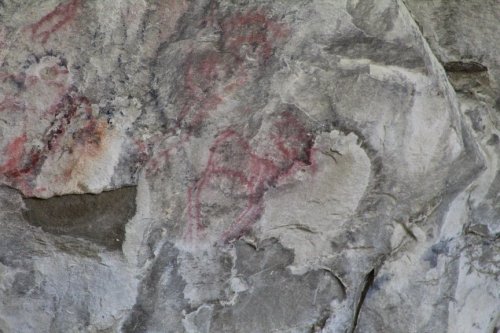 Ancient rock art featuring red markings on a textured stone surface.