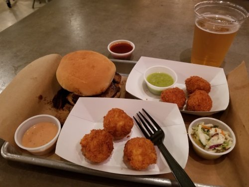 A tray with a burger, dipping sauces, fried balls, a side salad, and a glass of beer.