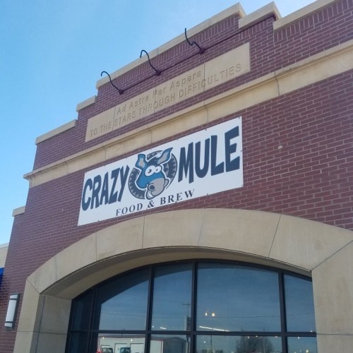 Sign for "Crazy Mule Food & Brew" on a brick building, with a blue sky in the background.