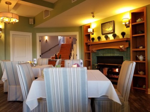 Cozy dining area with striped chairs, a fireplace, and warm lighting, featuring a staircase in the background.