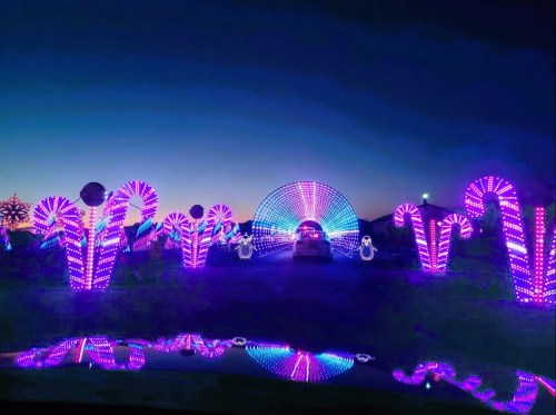 A colorful light display featuring pink and purple illuminated candy canes and arches against a twilight sky.