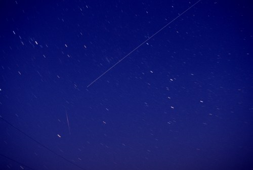 A night sky filled with stars, featuring streaks of light from meteors or satellites against a deep blue backdrop.