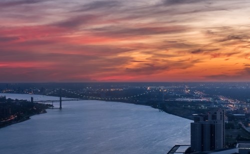 A scenic view of a river at sunset, with colorful clouds and city lights reflecting on the water.